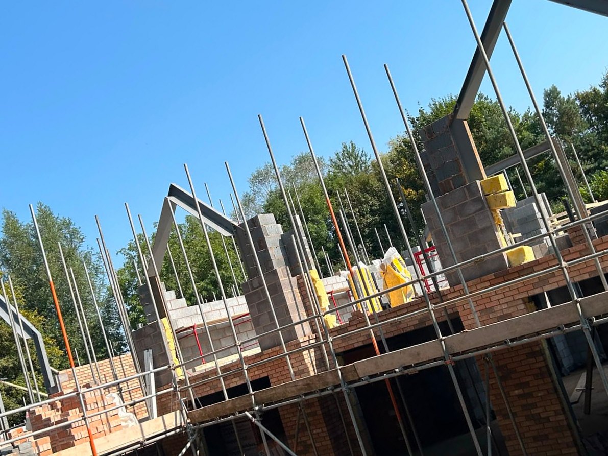 Steel gable frames and blockwork rising above the scaffold on a clear day