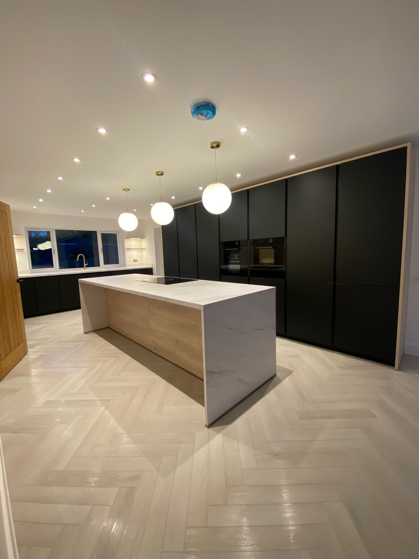 Open plan kitchen with marble topped island, black cabinetry and herringbone flooring
