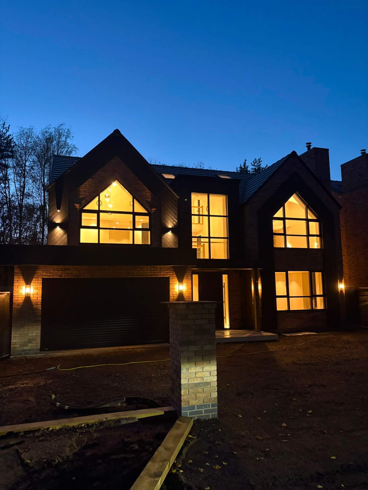 Bespoke gabled home at dusk with warm light glowing through full-height glazing