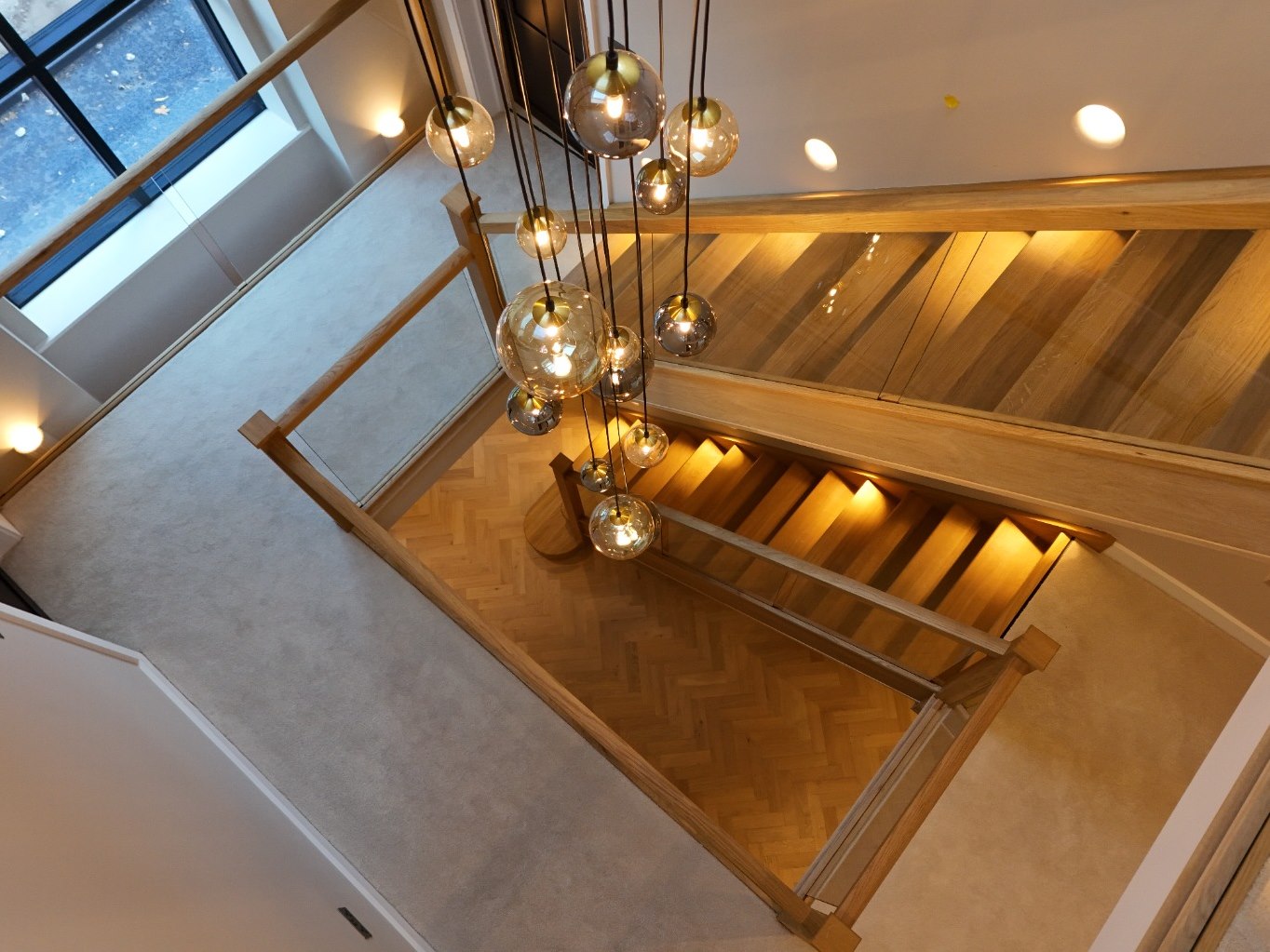 Cascading pendant lighting above the glass and oak staircase